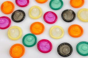 Des préservatifs de plusieurs couleurs déballés et disposés sur un support blanc